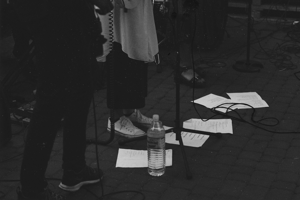 Foto in scala di grigi dei piedi di tre persone in piedi vicino alle aste dei microfoni