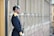 A uniformed guard stands at attention beside a building. The guard wears a dark blue uniform with gold accents and a shiny helmet with a spike on top. The guard holds a rifle with a bayonet attached, and appears to be standing in a formal posture.