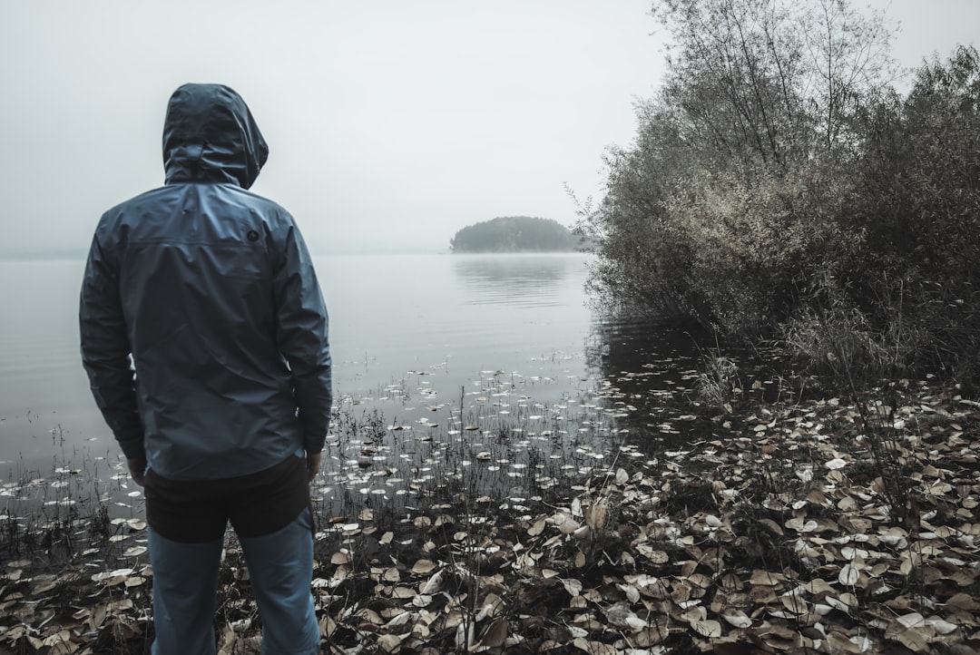 man in gray hooded jacket facing body of water