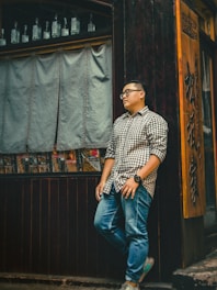 man in brown dress shirt leaning on wooden wall