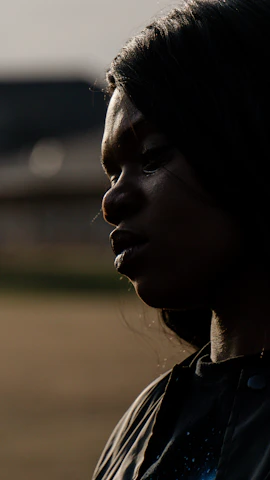 A dimly lit close-up of a contemplative face framed by shadows, evoking quiet introspection.