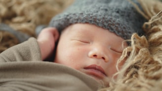 A peaceful sleeping baby is nestled in cozy, soft brown and beige textures, wearing a knitted gray hat.