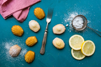 A rustic shot of lemon madeleines dusted with powdered sugar, set against a deep charcoal background.