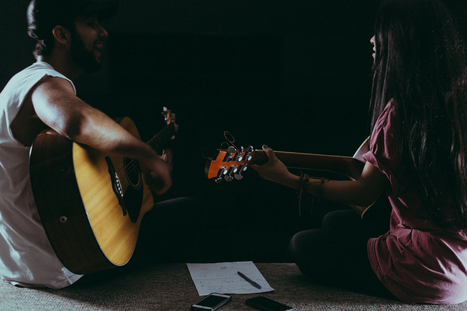 Two adults practising guitar together in a warm-lit room