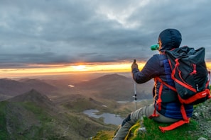 A traveler holding a rajiree water bottle overlooking a scenic mountain vista during sunset.