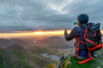 A traveler holding a rajiree water bottle overlooking a scenic mountain vista during sunset.