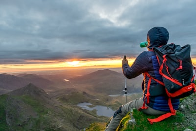 man sitting on cliffhanger looking at mountain under gloomy clouds successful teams background