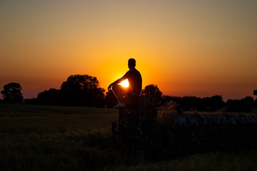 a man standing in a field with the sun setting behind him