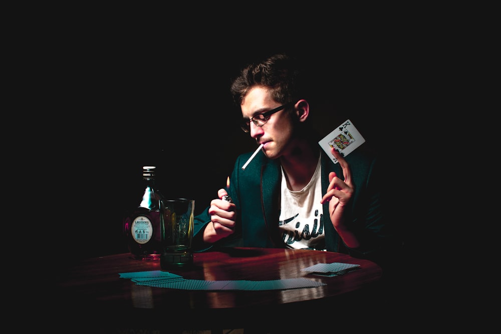man lighting cigarette while holding playing card