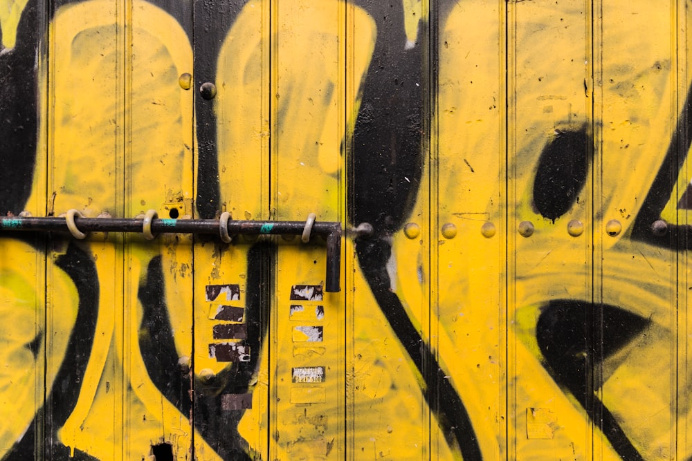 yellow and black wooden gate with graffiti and metal pole