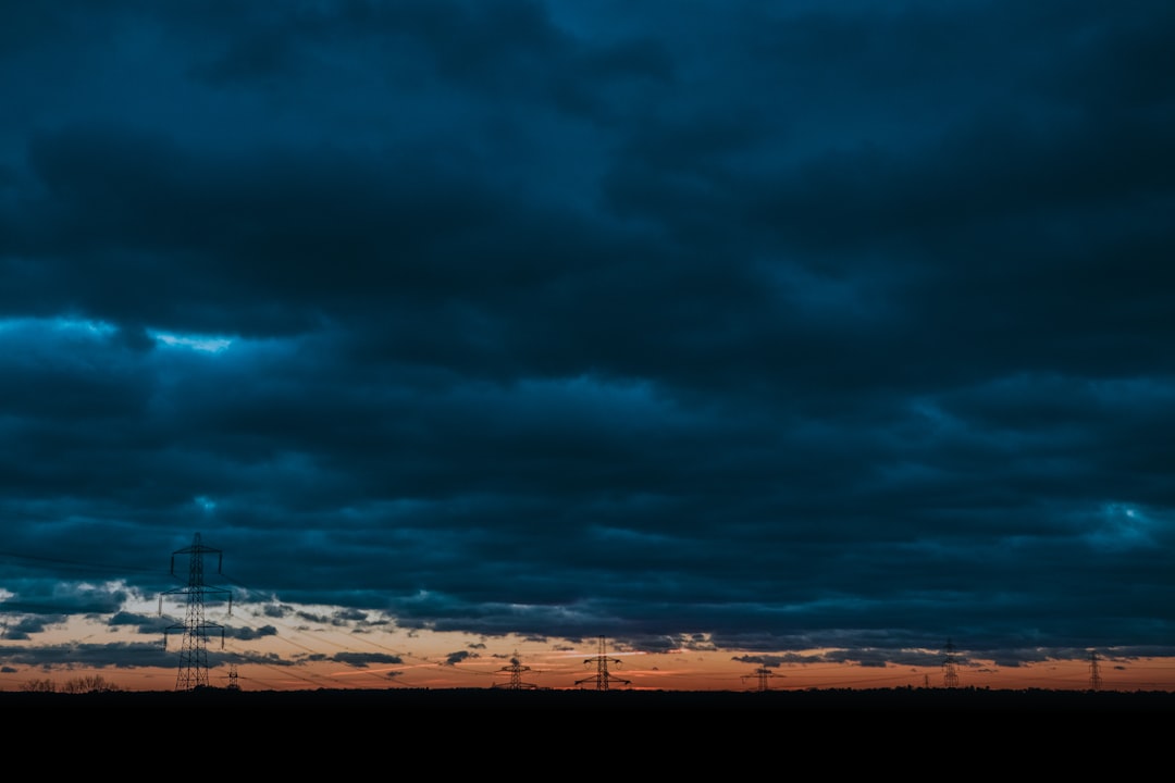 silhouette photo of transmission towers under cloudy skiy