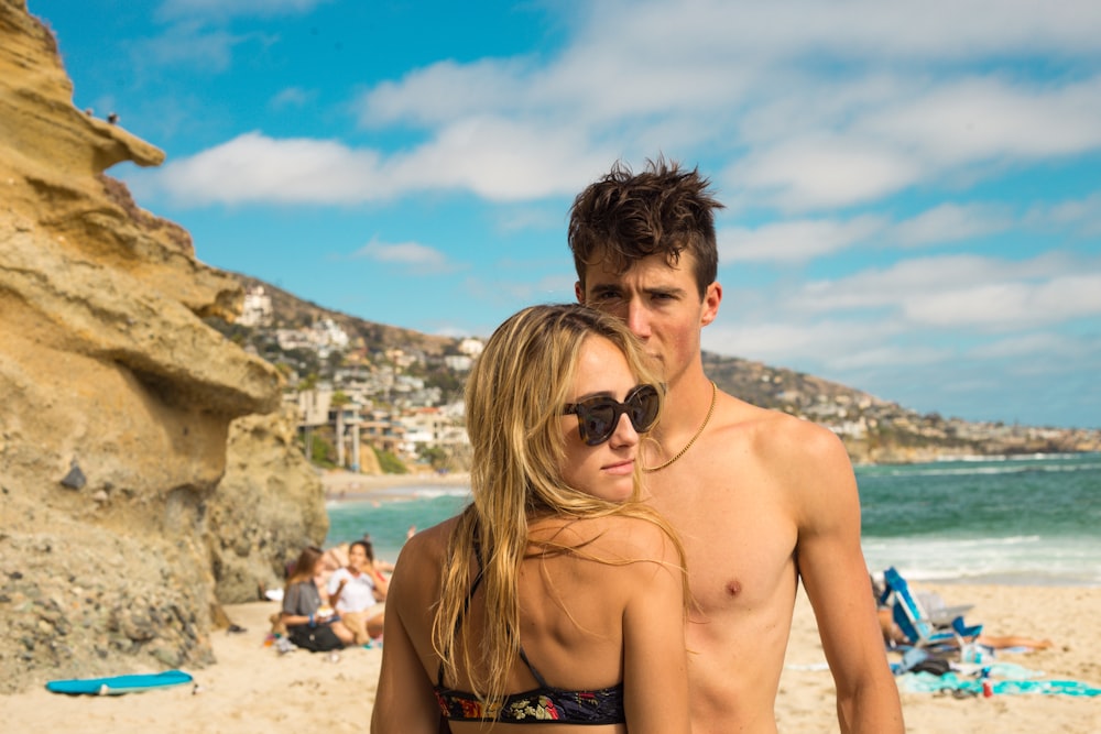 woman wearing sunglasses and bikini front of man standing near seashore