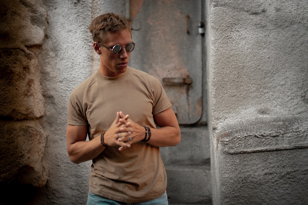 man in brown t-shirt sitting beside metal door and gray concrete wall
