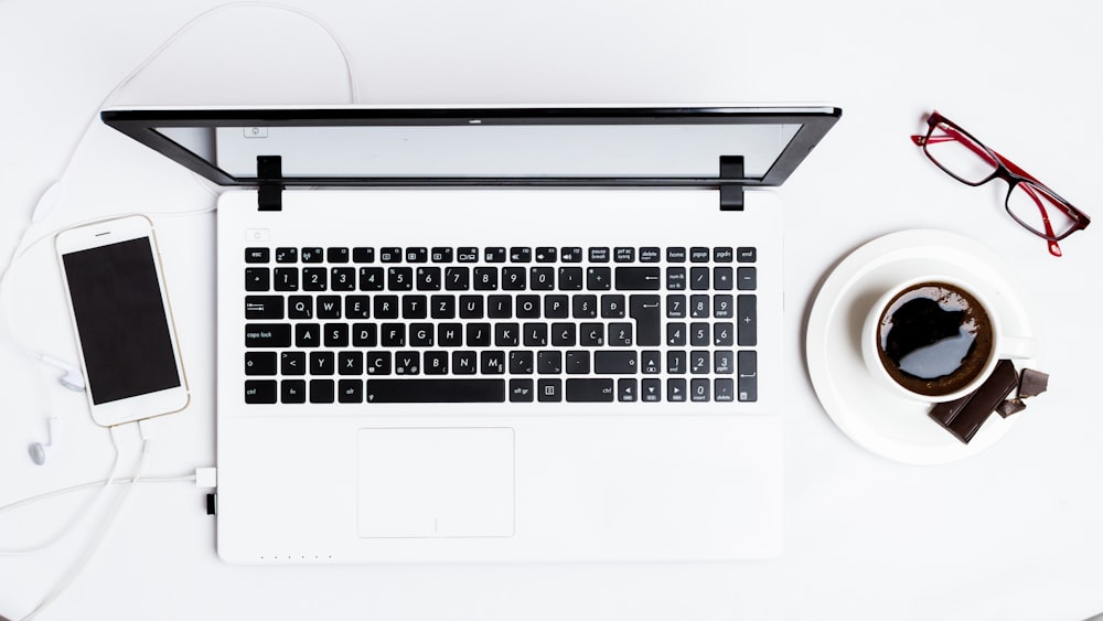 MacBook Pro between smartphone and teacup on white surface