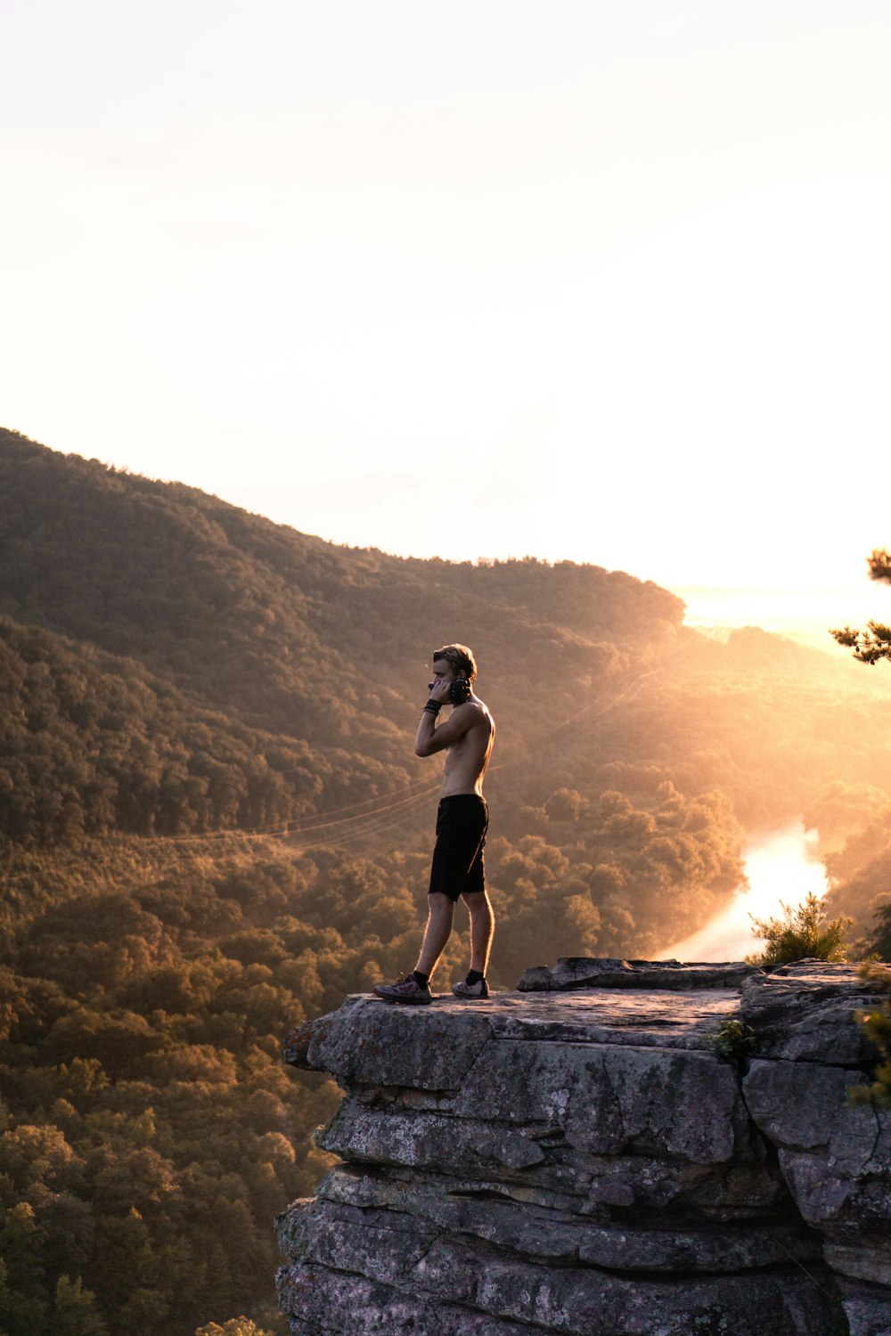 man in black shorts standing on cliff during golden hour