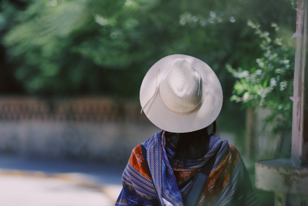 Person mit grauem Fedora-Hut in der Nähe von grünen Laubbäumen während des Tages