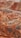 A vibrant and colorful landscape features layered hills and mountains with distinct striations of red, orange, and yellow hues. The terrain is rugged and undulating with a lone bus traveling on a narrow road that winds through the unique geologic formations.