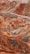 A vibrant and colorful landscape features layered hills and mountains with distinct striations of red, orange, and yellow hues. The terrain is rugged and undulating with a lone bus traveling on a narrow road that winds through the unique geologic formations.