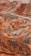 A vibrant and colorful landscape features layered hills and mountains with distinct striations of red, orange, and yellow hues. The terrain is rugged and undulating with a lone bus traveling on a narrow road that winds through the unique geologic formations.