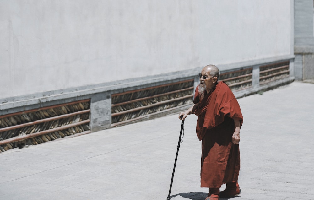 monk walking while holding cane near white wall