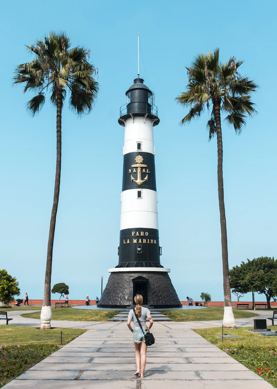 Woman walking towards a white-painted lighthouse with two palm trees on either side