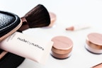 A collection of cosmetics is neatly displayed, including a makeup brush, a black zippered pouch, and several rose-gold capped jars. A tube that reads 'nude by nature' is partially visible, suggesting a beauty product brand.