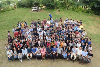 A group photo of diverse community members seated comfortably on the grass, framed by gentle greenery.