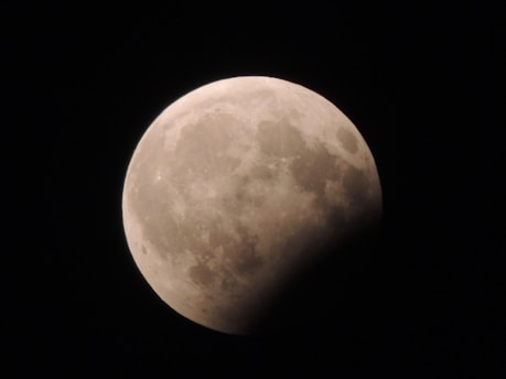A partially eclipsed moon with a shadow covering a portion of its surface, set against a dark night sky.