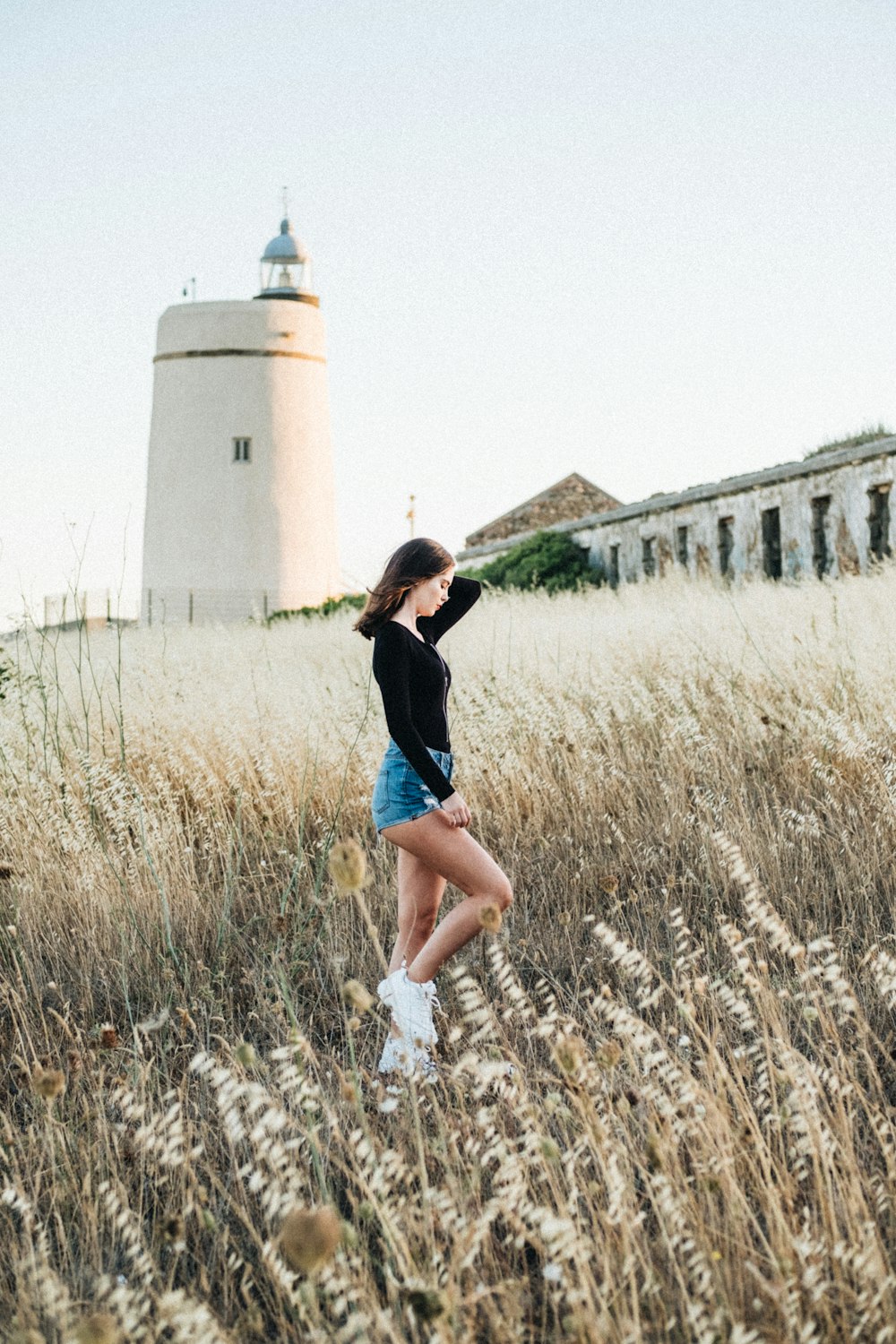 woman in black shirt and blue denim shorts walking on brown grass field during daytime