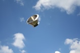 A stainless steel kitchen colander is floating in a bright blue sky with scattered white clouds.