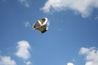 A stainless steel kitchen colander is floating in a bright blue sky with scattered white clouds.