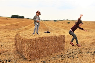 Children playing games on the farmhouse lawn surrounded by hay bales and colorful bunting.