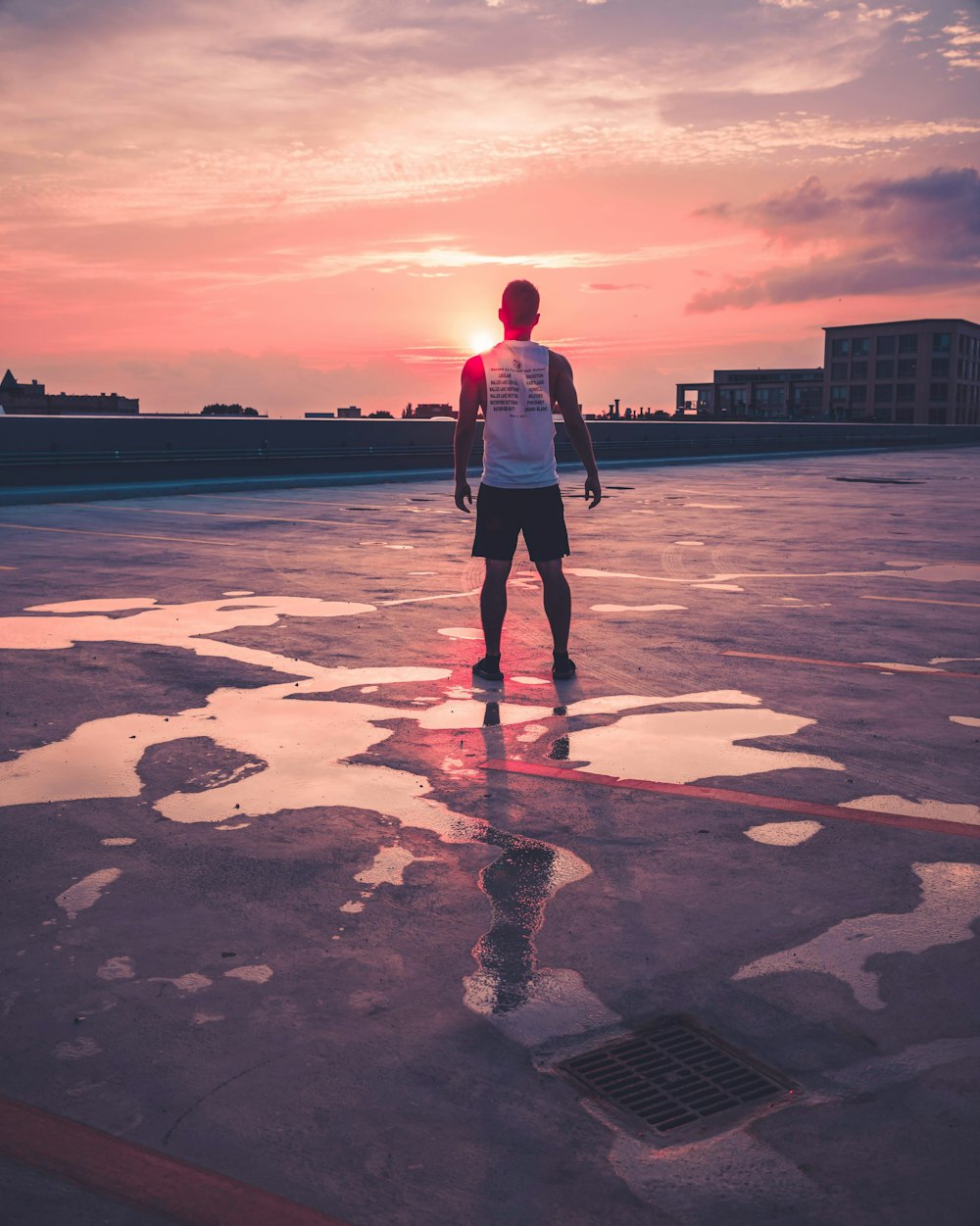 man standing above gray concrete area facing large buildings at golden hour