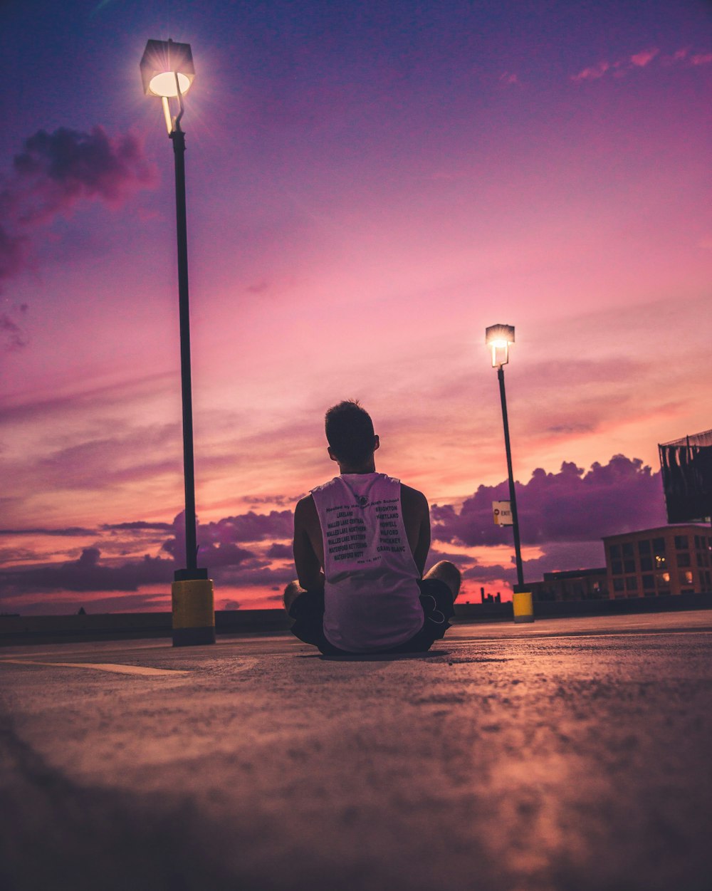 man sitting on road near turned-on black post lamp during sunset