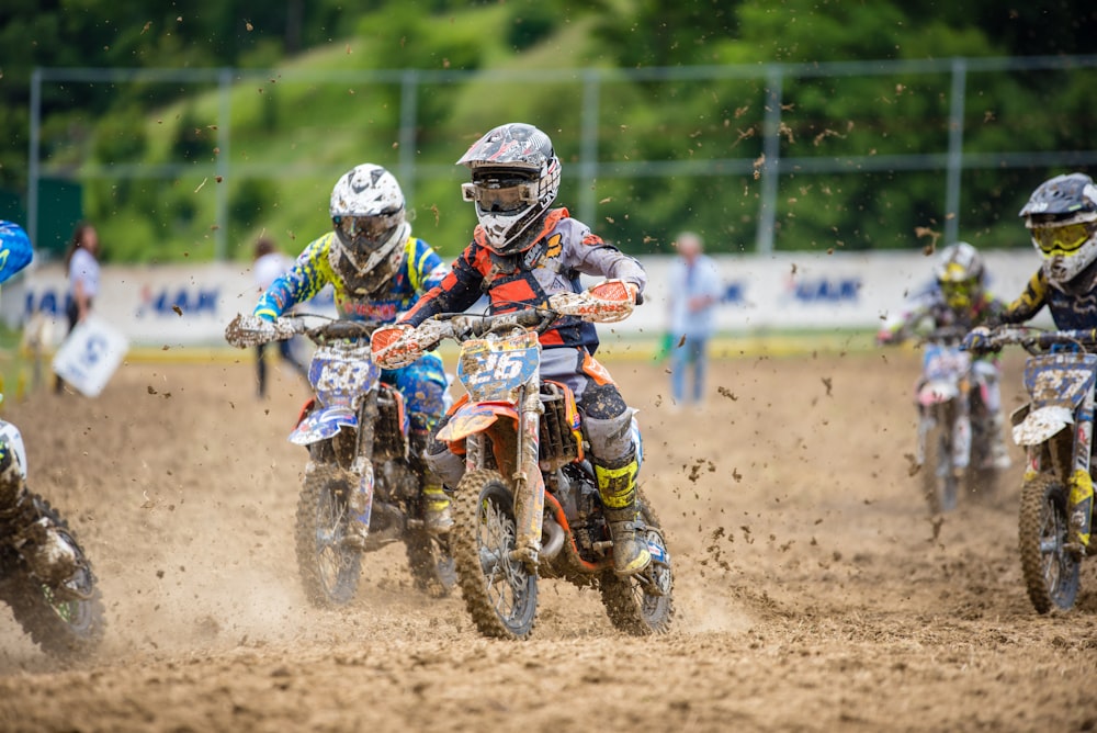 five riders riding motocross dirt bike on muddy race track at daytime
