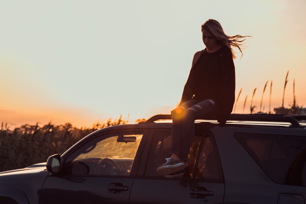 Frau sitzt auf dem Fahrzeugdach aufgenommen während der goldenen Stunde