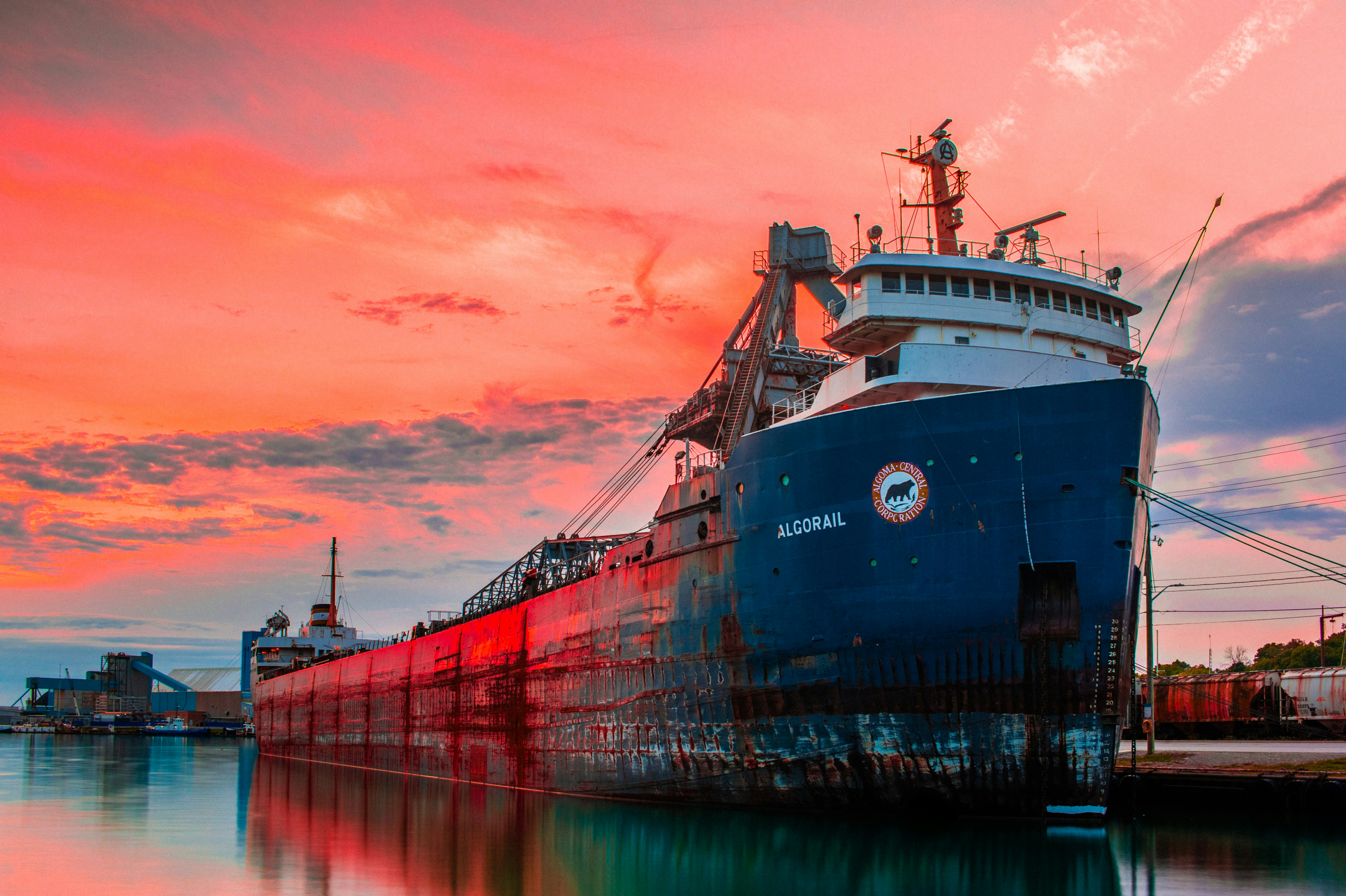 A professional cargo ship docked at a busy international port during sunset.