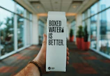 person holding boxed water is better box