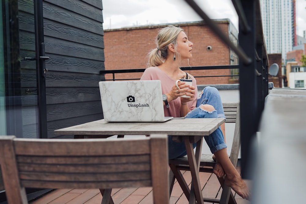 woman sitting on gray wooden chair beside rectangular table with white laptop at daytime