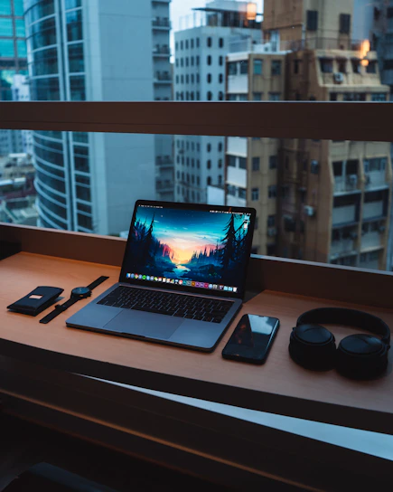 A welcoming office desk with a laptop, notebook, and a cup of coffee beside a window showing a city skyline.