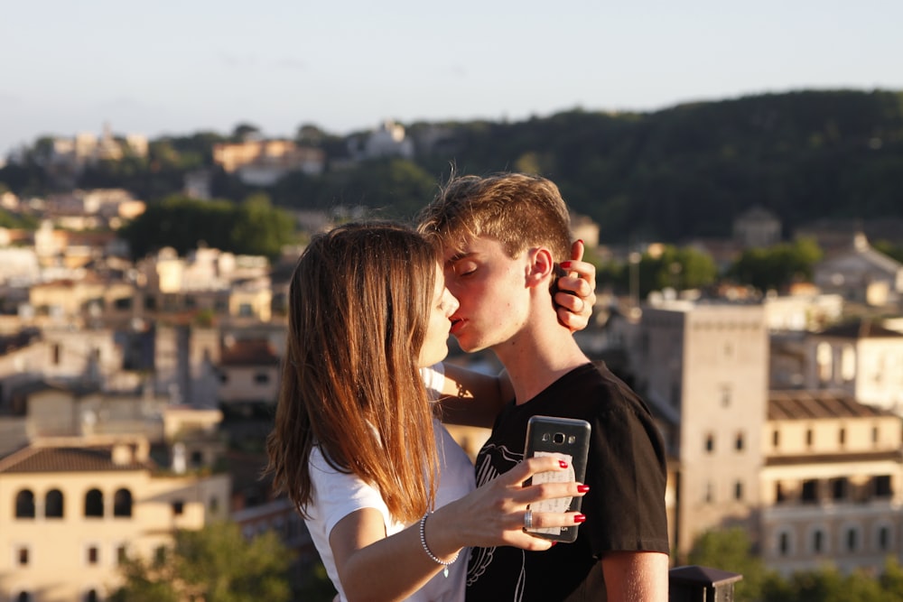 woman try to kiss man while holding smartphone