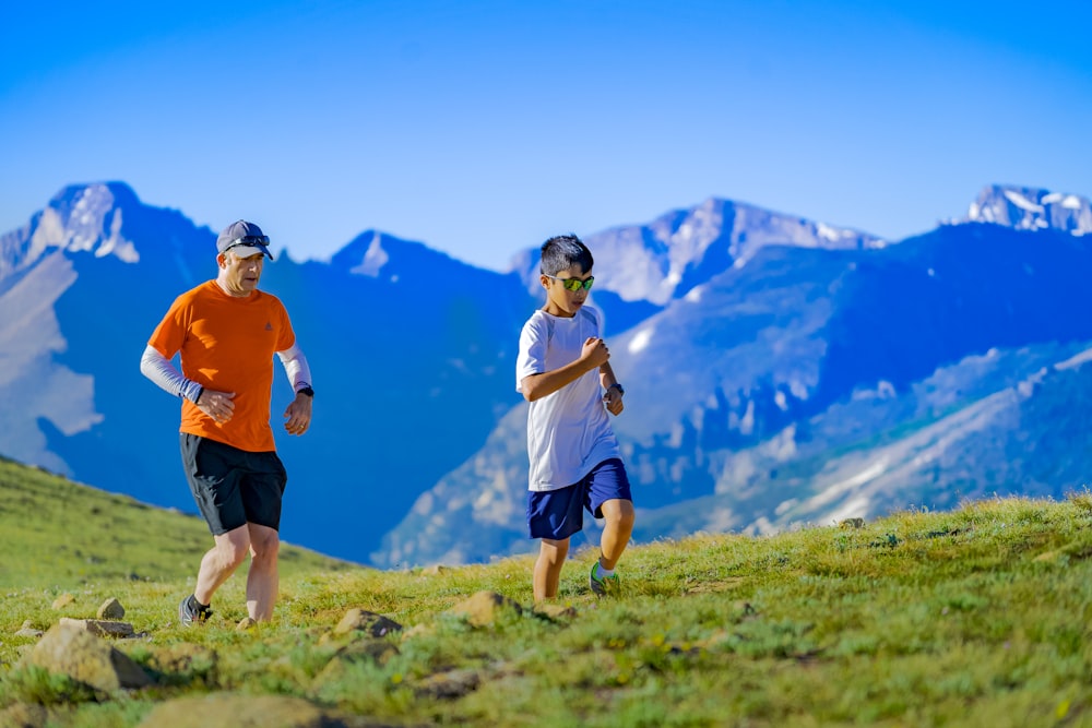 man and boy running on green grass field at daytime