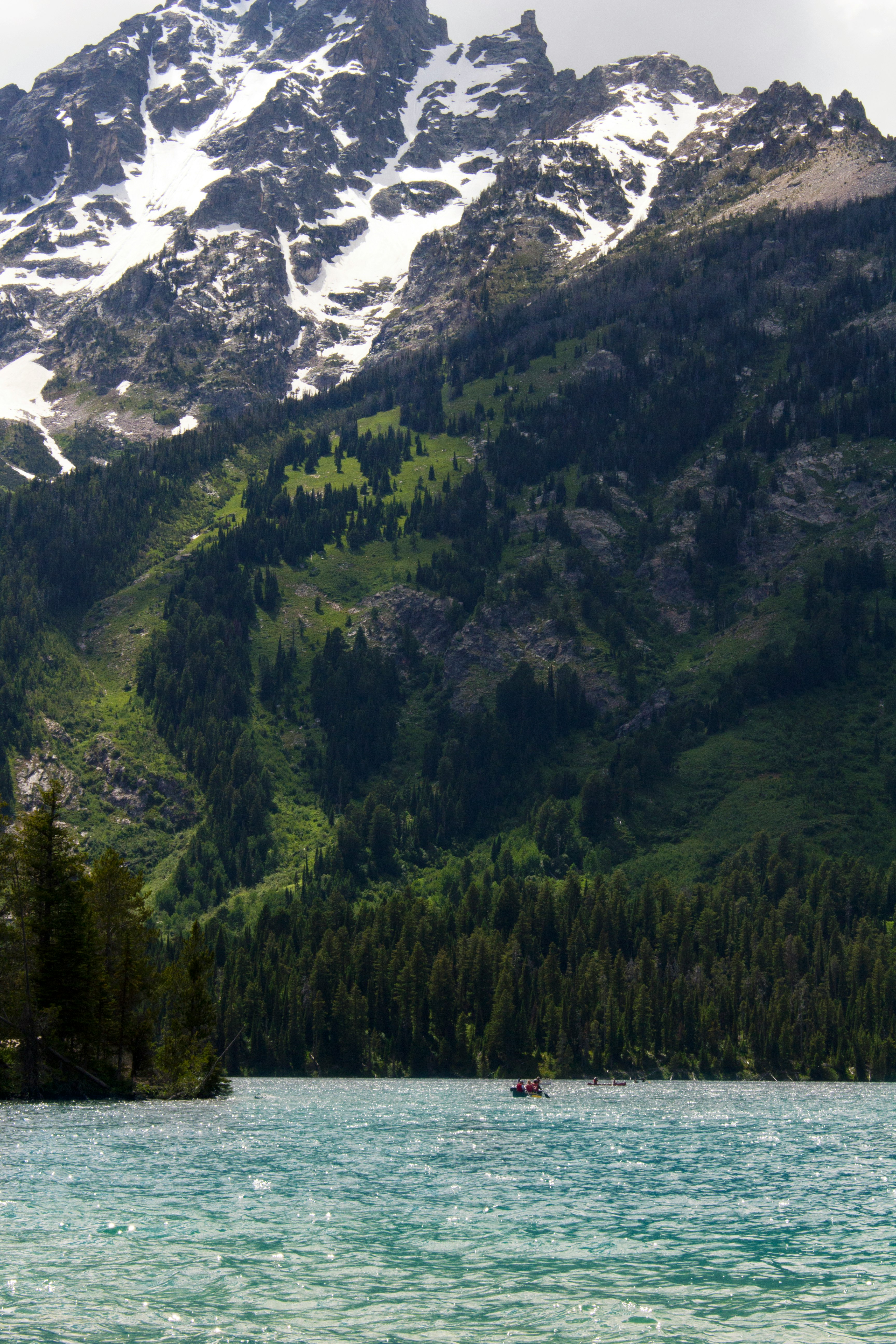 blue body of water near green hill and snow-covered mountain under cloudy sky