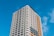 A tall, modern apartment building with many floors and a mix of grey and light brown facade panels, set against a clear blue sky. The windows are lined in rows, typical of a residential high-rise.