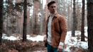 man wearing white turtleneck sweater with brown jacket while standing in forest