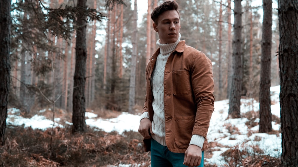 man wearing white turtleneck sweater with brown jacket while standing in forest