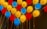 A colorful arrangement of illuminated balloons in red, yellow, and blue, affixed to a wall. The balloons create a vibrant and festive atmosphere, with strings attached to each balloon.