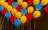 A colorful arrangement of illuminated balloons in red, yellow, and blue, affixed to a wall. The balloons create a vibrant and festive atmosphere, with strings attached to each balloon.