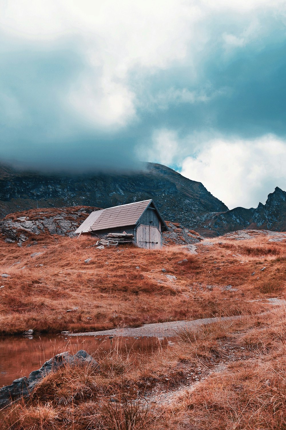 brown and gray wooden barn on brown grass field under cloudy sky at daytime