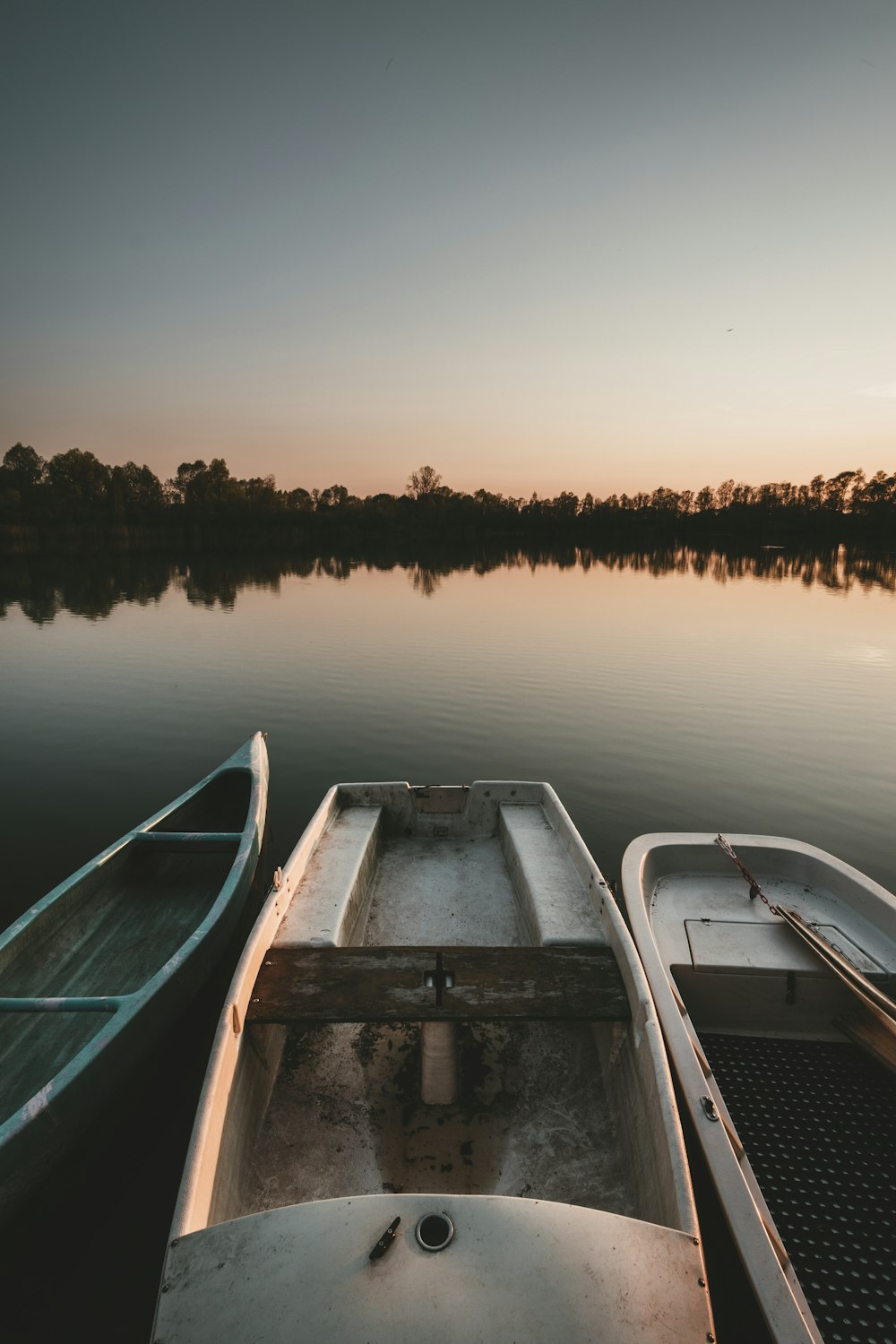 three white boats on lake in front of silhouette of trees